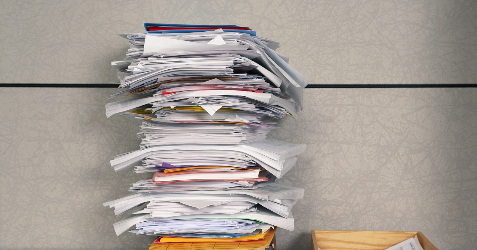 Przepełniona taca „IN BOX” z górą dokumentów obok pustej tacy „OUT BOX” — obraz biurokracji, która narasta szybciej, niż da się ją rozliczyć.